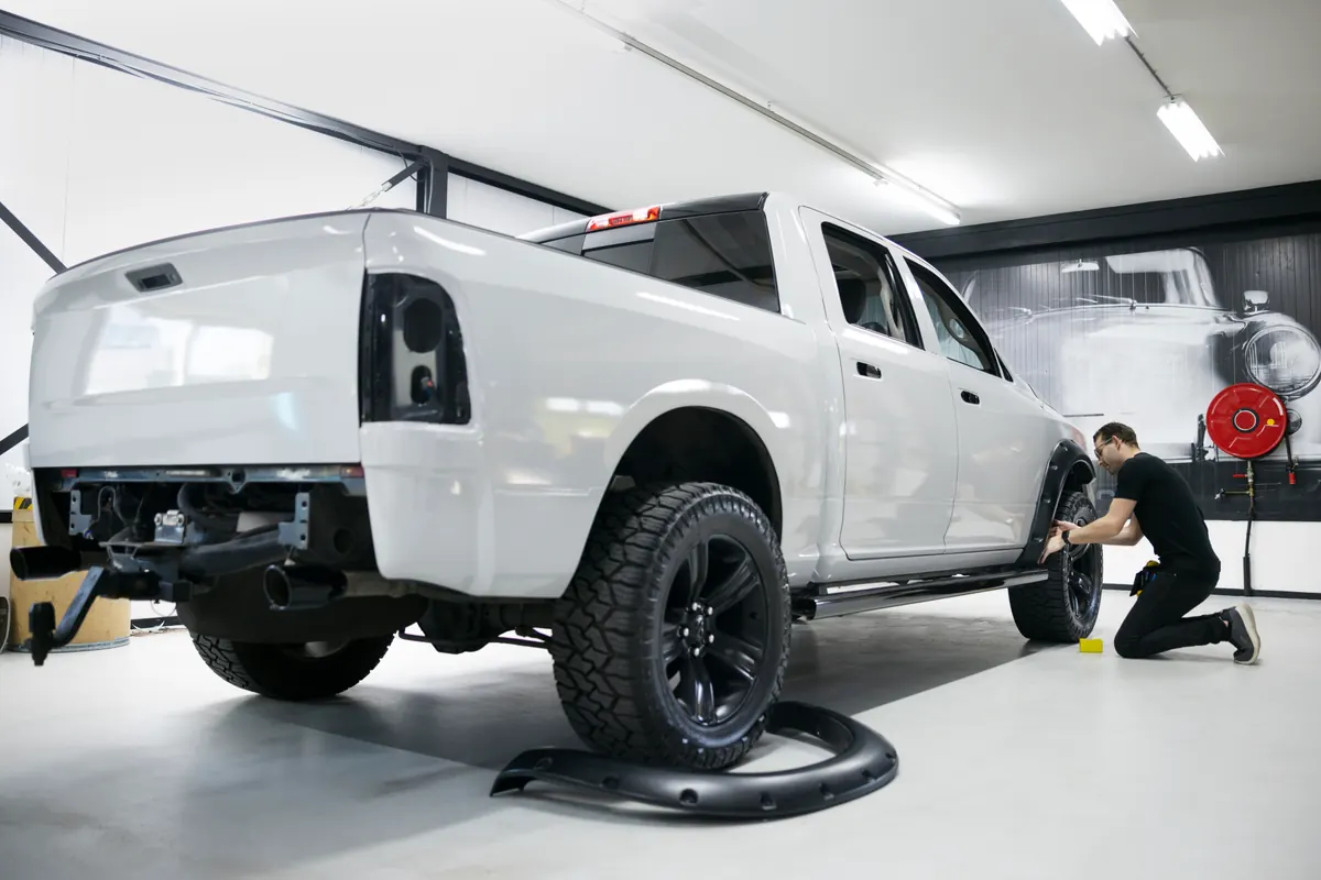 Pickup truck in a shop bay while a technician works on its wheel