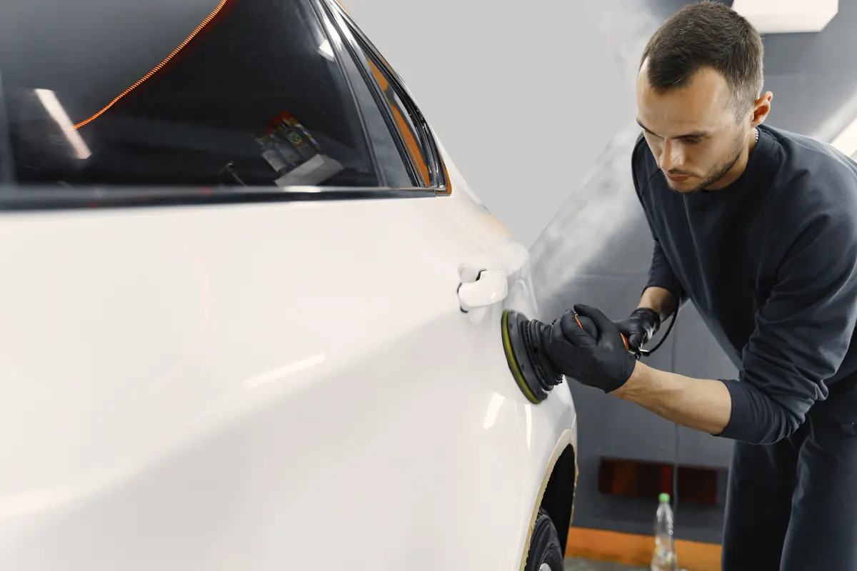 Technician polishing the door of a white car with a machine polisher